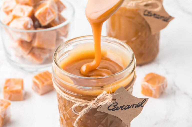 A spoon drizzling caramel sauce in a jar.