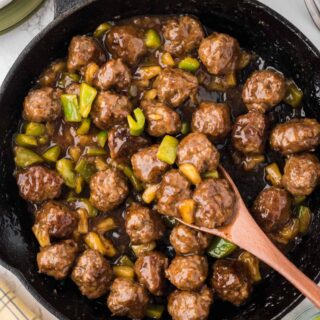 Waikiki meatballs in a skillet with a wooden spoon.