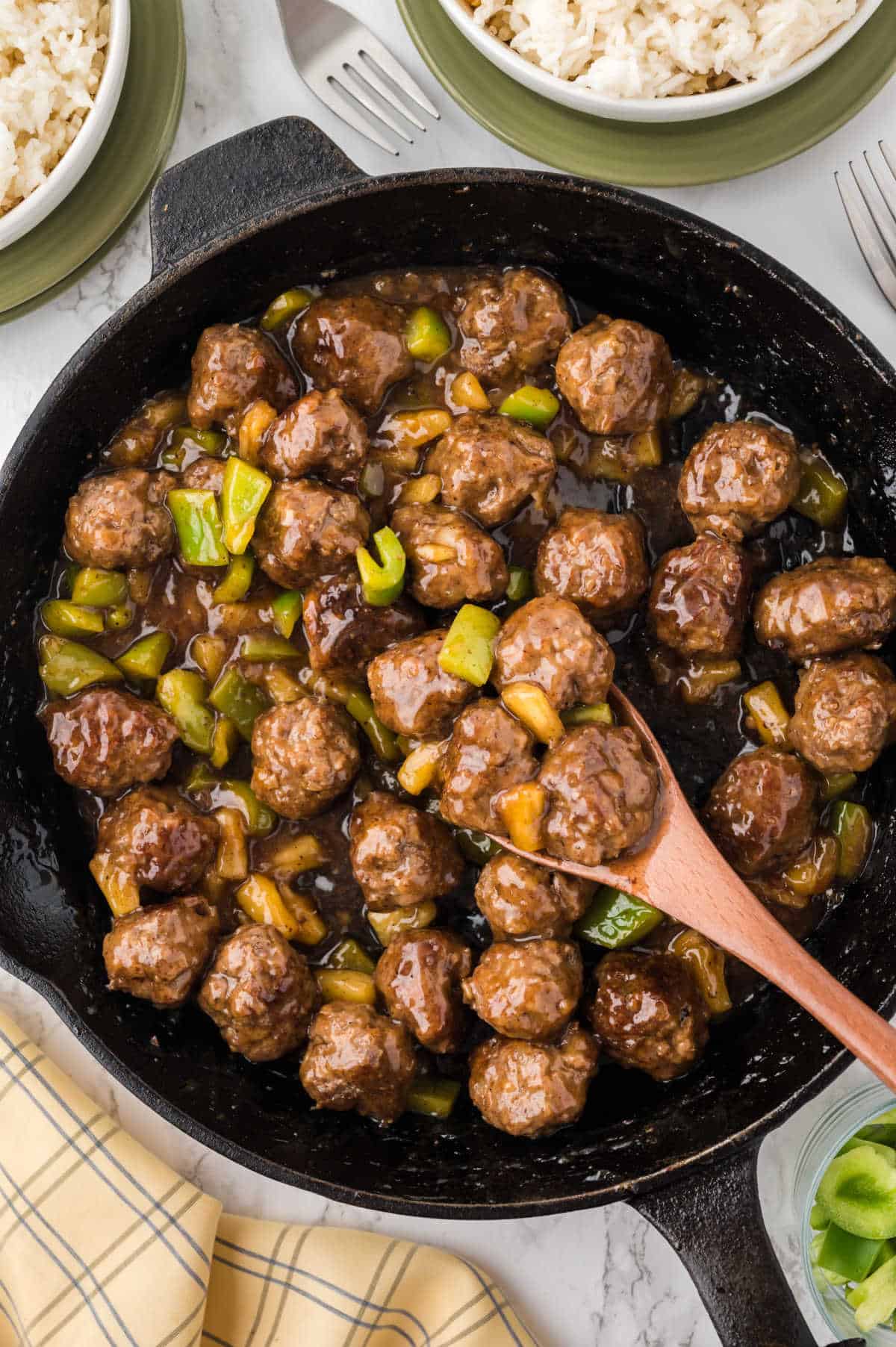 Waikiki meatballs in a skillet with a wooden spoon.