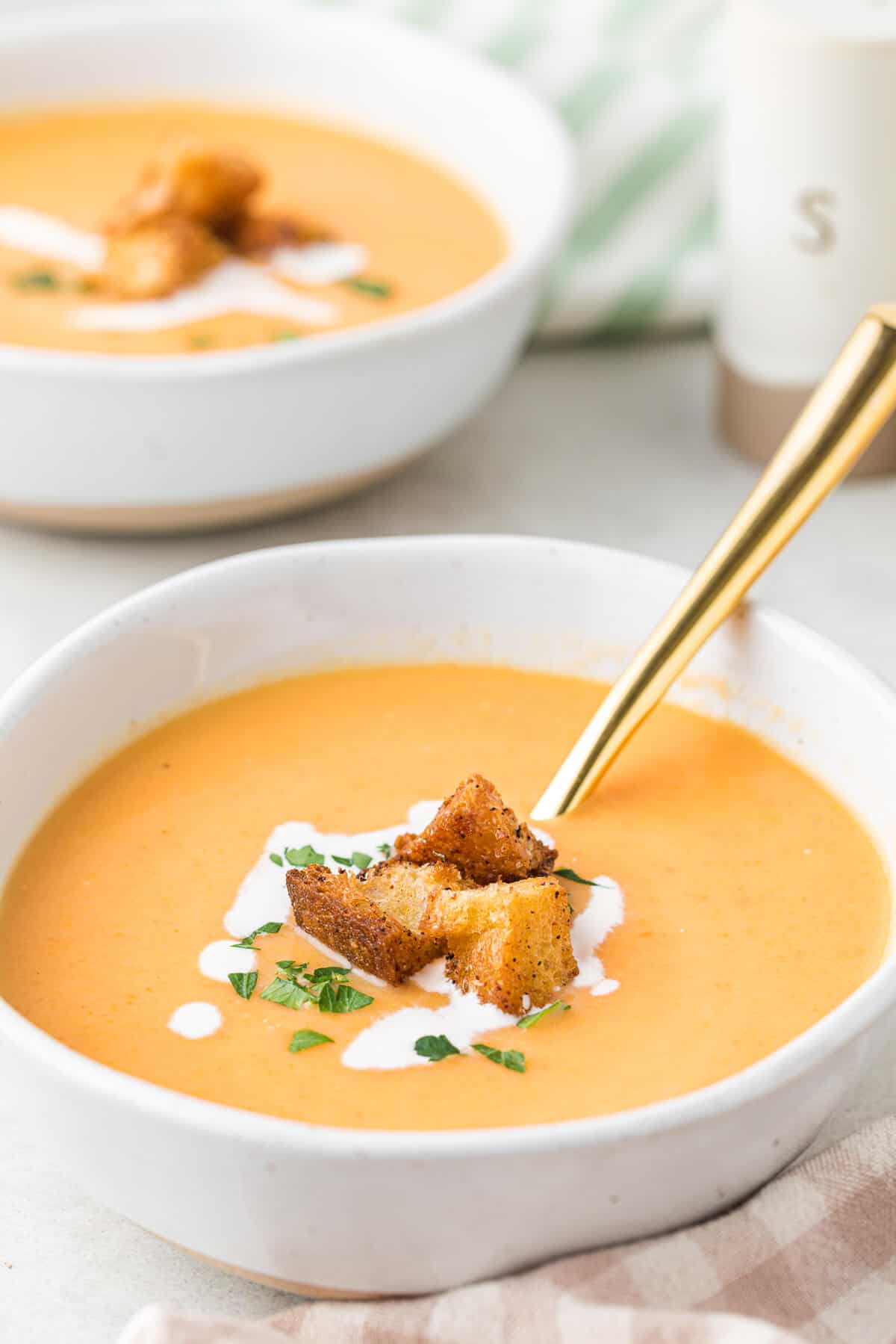 A bowl of cream of carrot soup topped with croutons and a gold spoon in the soup.
