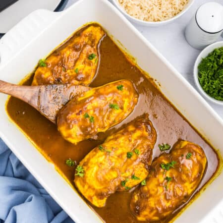 Honey curried chicken in a pan with a serving spoon.