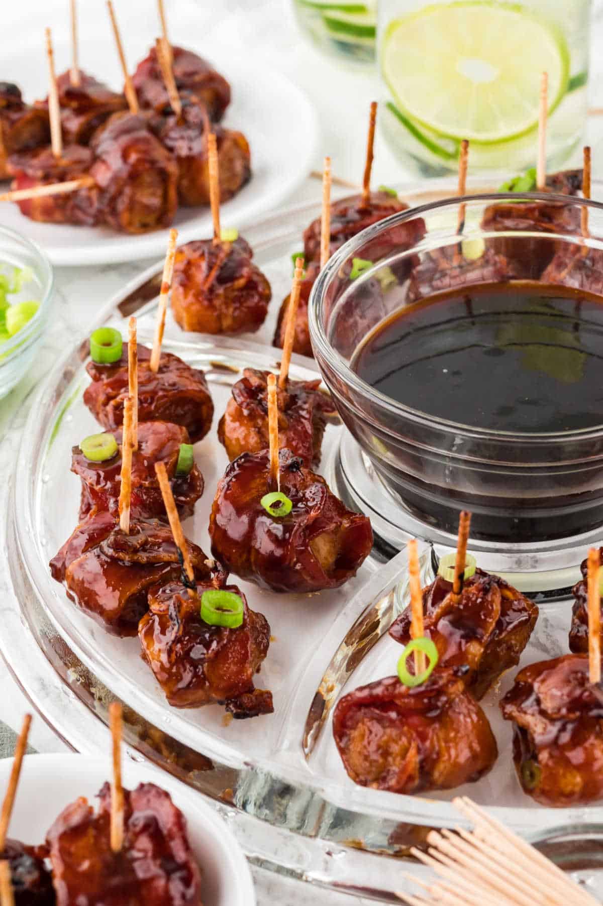 Bacon wrapped water chestnuts on a platter with dipping sauce.