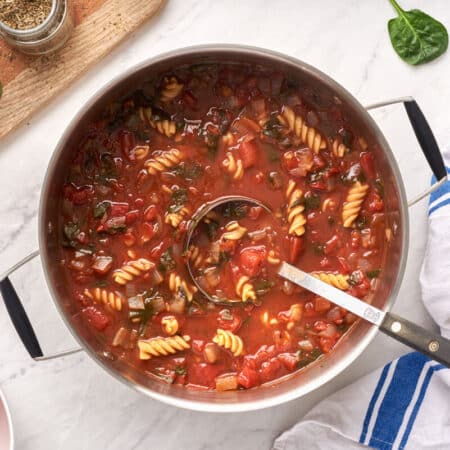 A pot of tomato florentine soup with a ladle.