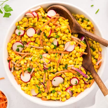 Corn salad in a bowl with wooden spoons.