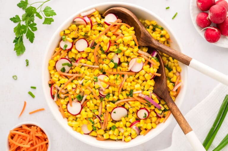 Corn salad in a bowl with wooden spoons.