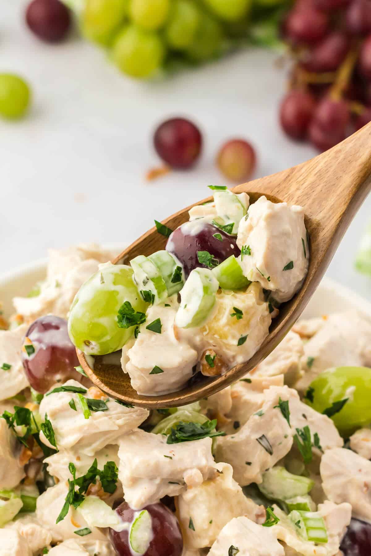 Chicken salad with grapes on a wooden spoon.
