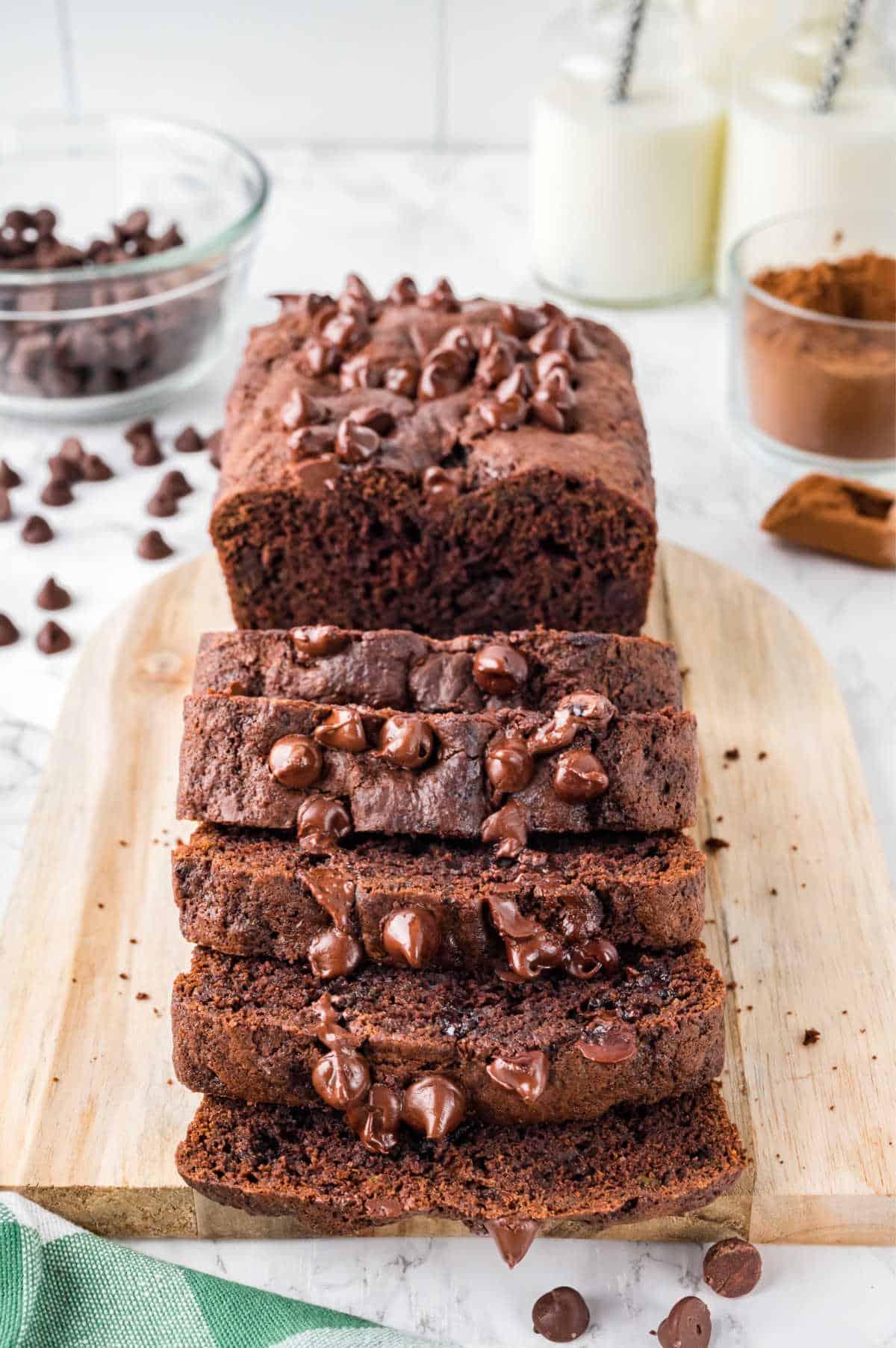 A loaf of chocolate zucchini bread partially cut into slices on a wooden cutting board.