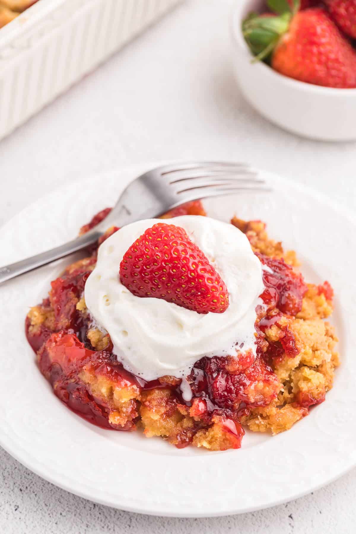 Strawberry Dump cake on a plate topped with whipped cream and a strawberry