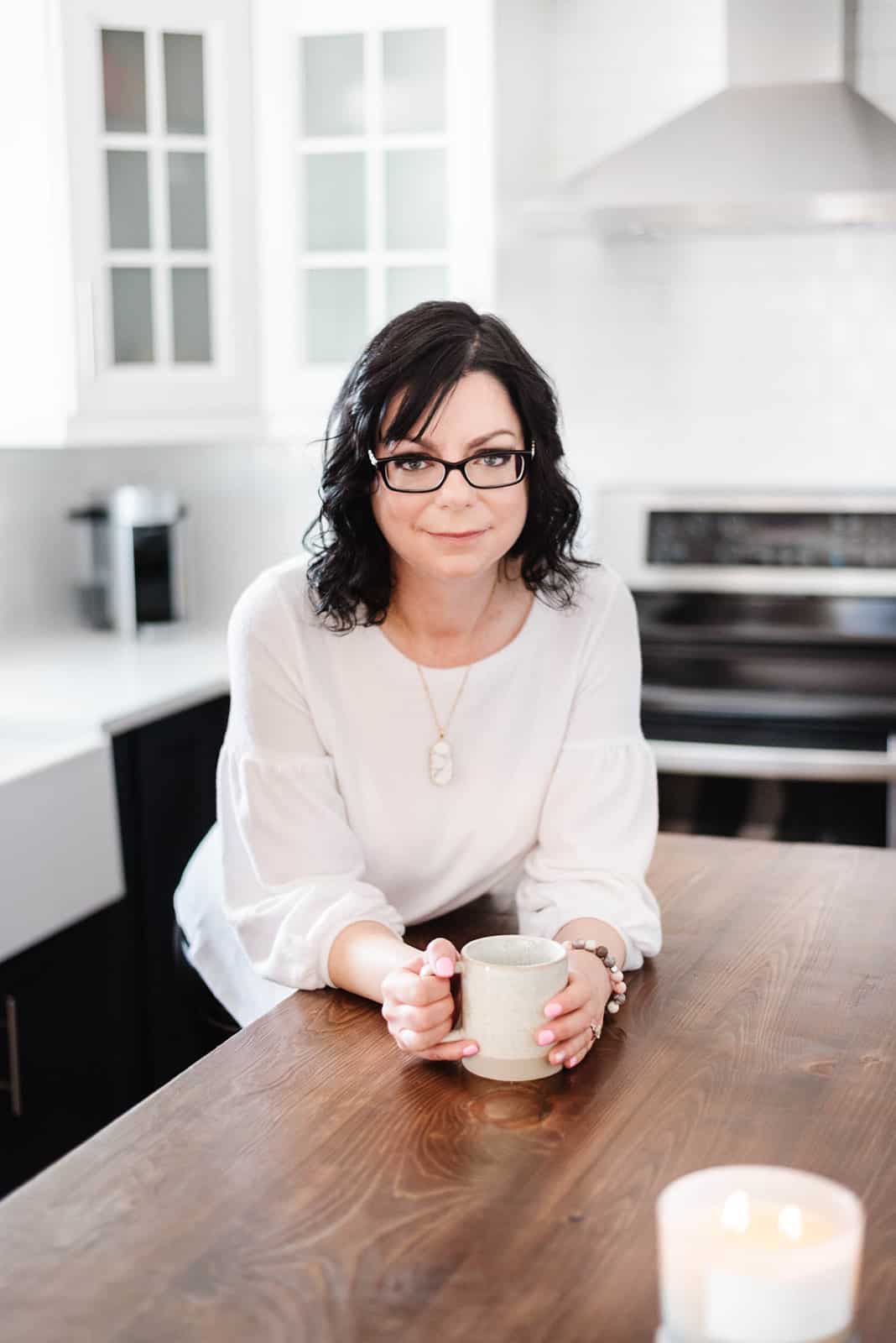 Food blogger Stacie Vaughan holding a coffee cup on a kitchen counter.