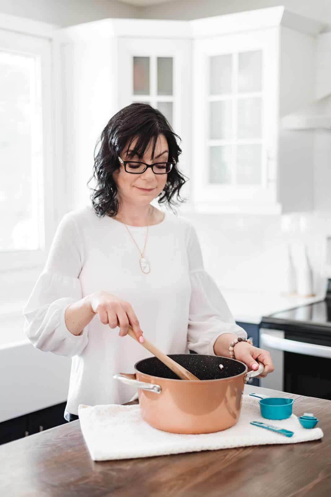 Food blogger Stacie Vaughan stirring a copper pot on a wooden counter.