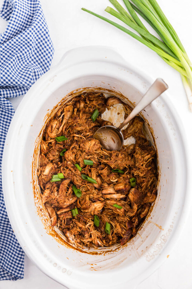 Chicken in a white crockpot with a serving spoon.