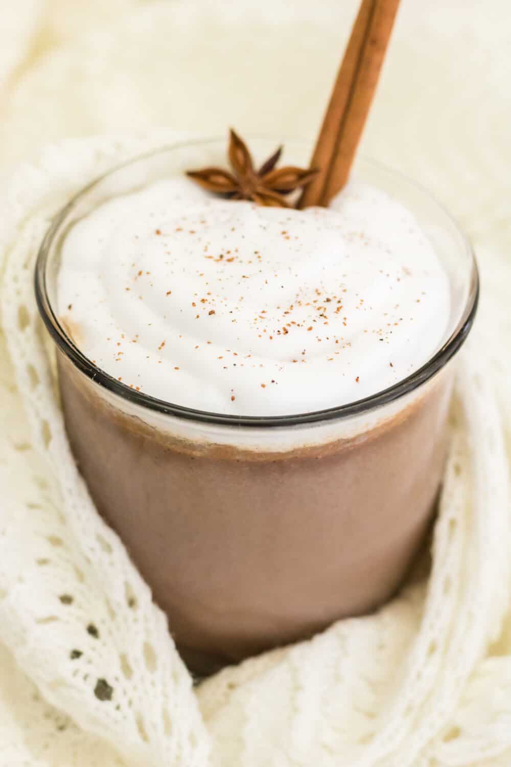 cinnamon hot chocolate in a glass mug wrapped in a cream knitted blanket
