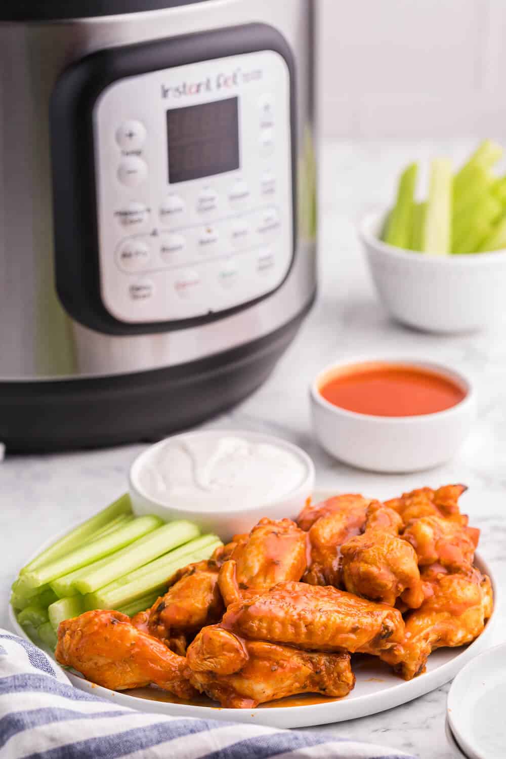 A plate of buffalo chicken wings with celery and dip and an air fryer in the background