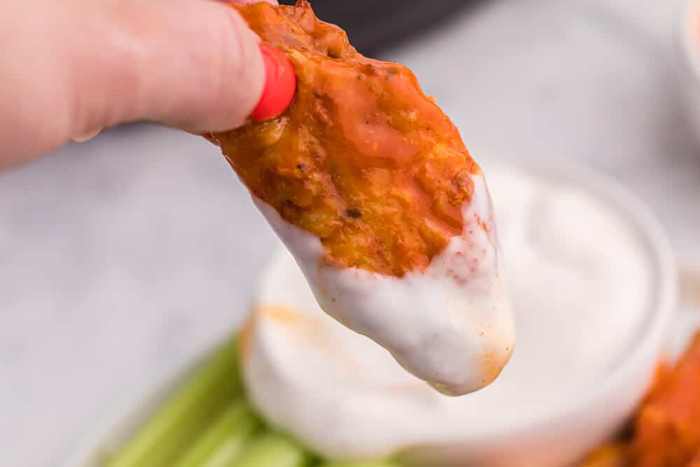 A hand holding a buffalo chicken wing with ranch dip on it