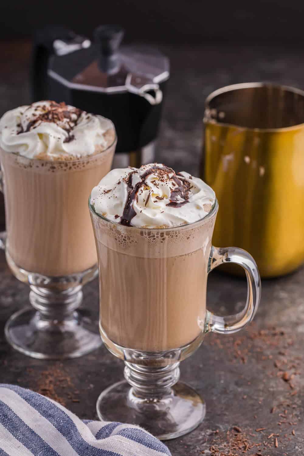 two mugs of mocha latte with an espresso maker and a milk frothing pitcher