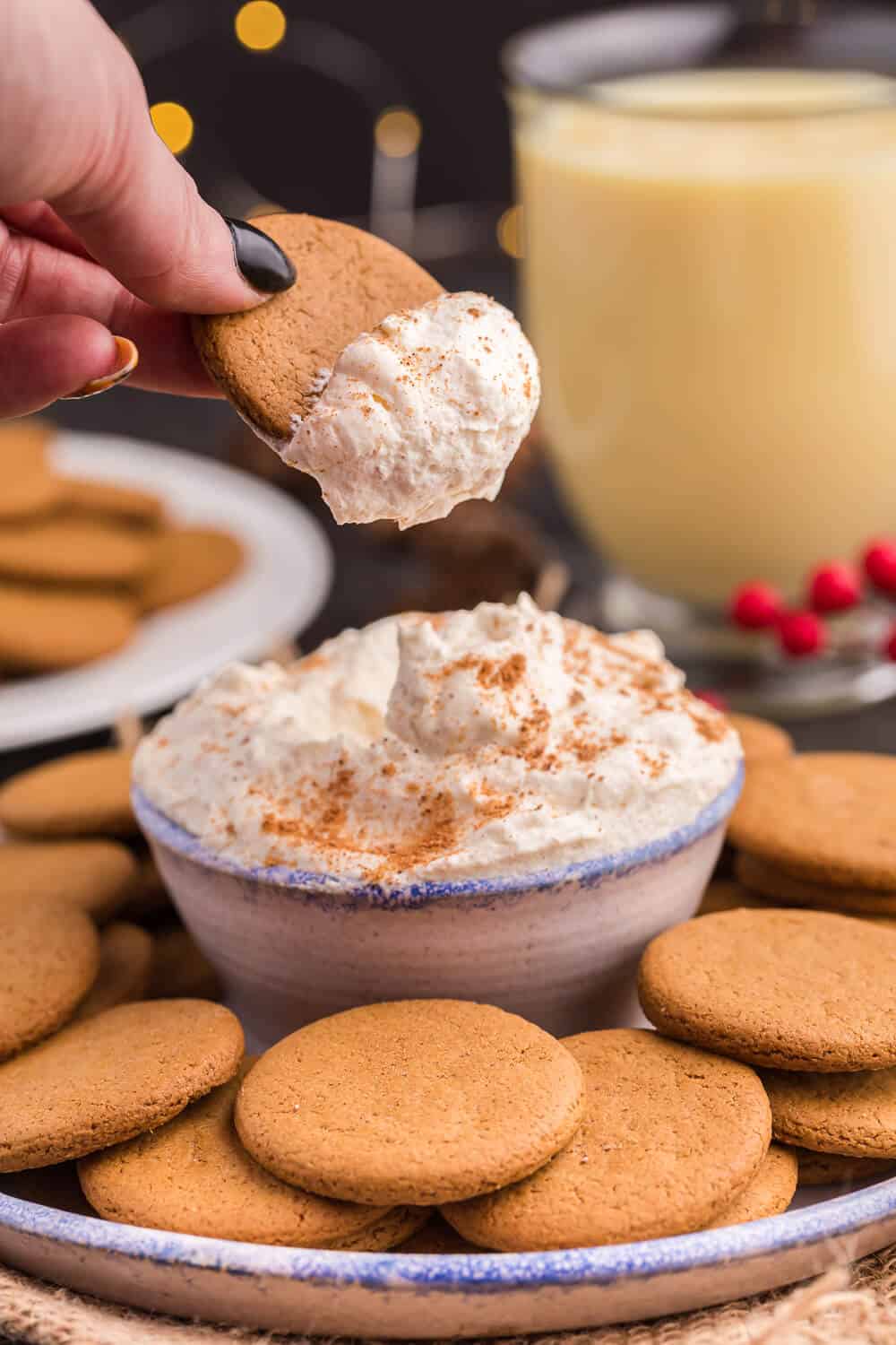 A hand holding a gingersnap cookie with eggnog dip on it