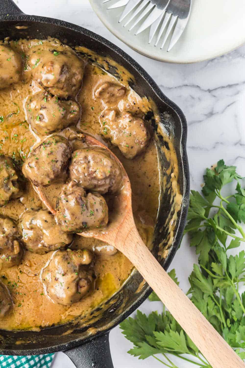 swedish meatballs in a cast iron skillet with a wooden serving spoon