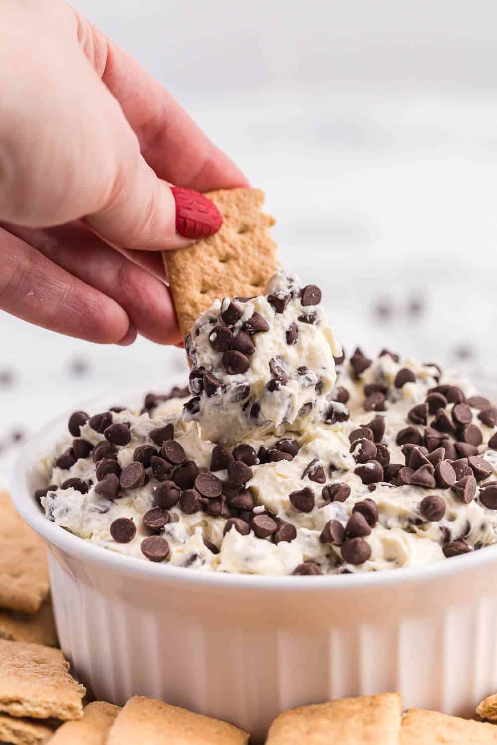 A hand dipping a graham cracker into the recipe.