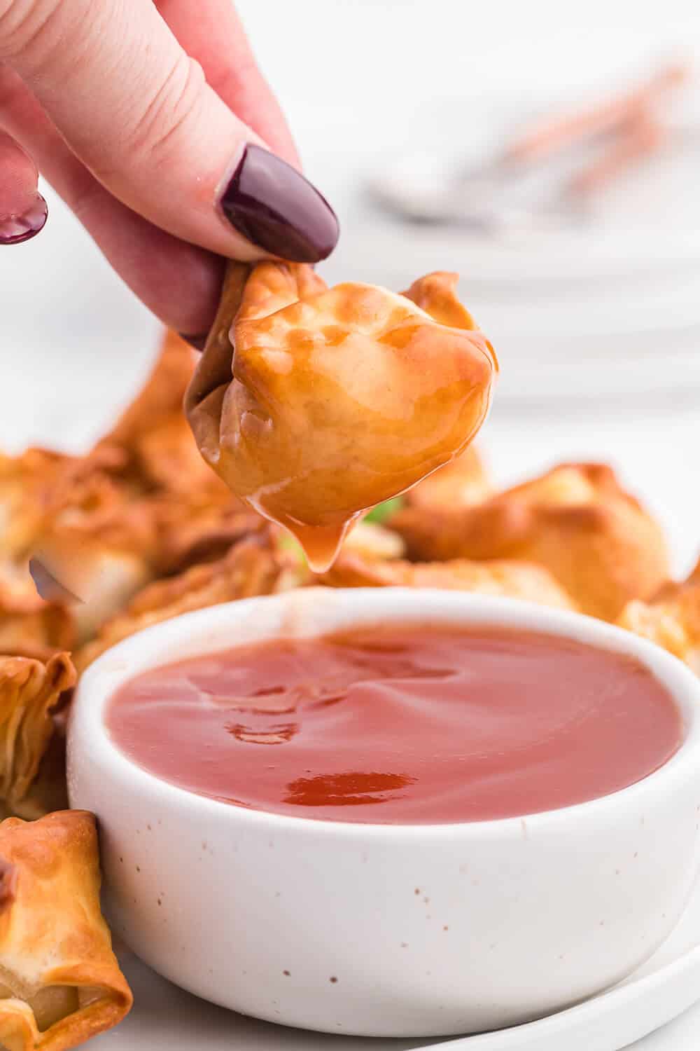 a hand dipping an air fryer crab rangoon in sweet and sour sauce