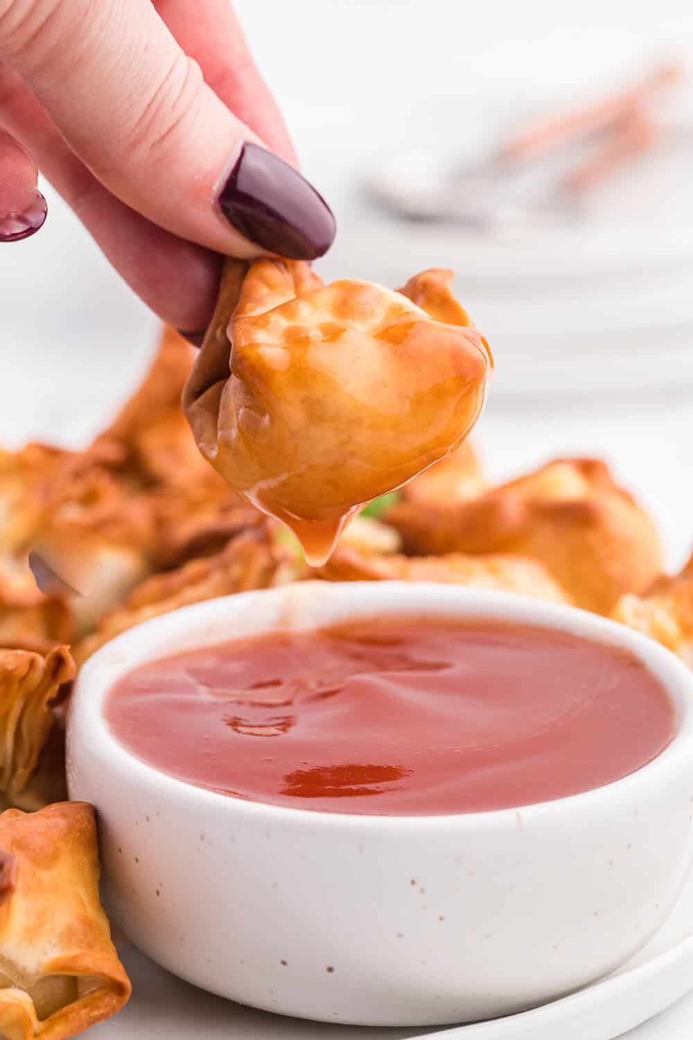 A hand dipping the recipe in sweet and sour sauce.
