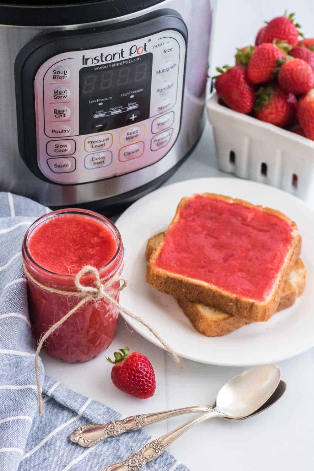 Instant pot strawberry jam in a mason jar beside two slices of toast with jam.