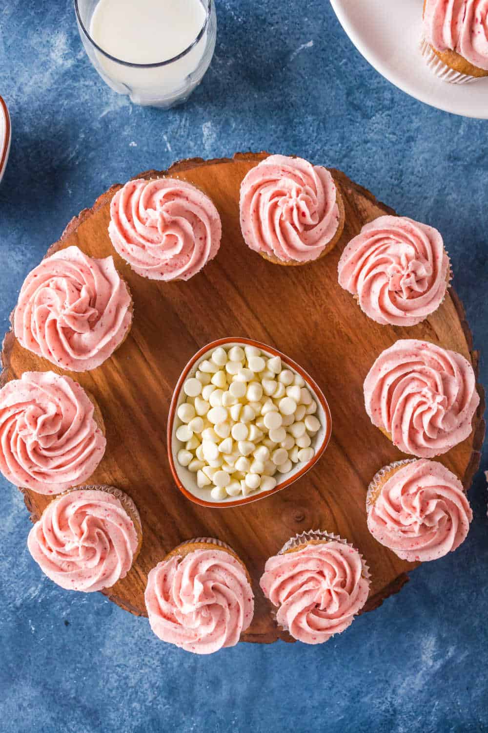 strawberry cupcakes on a circular wooden platter with a bowl of white chocolate chips