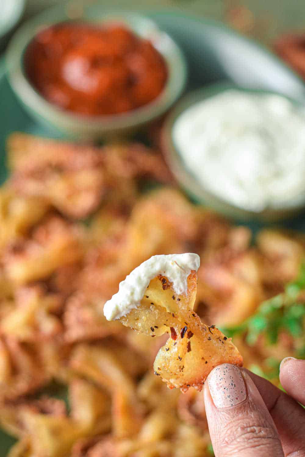 A hand holding a pasta chip with feta dip on it.