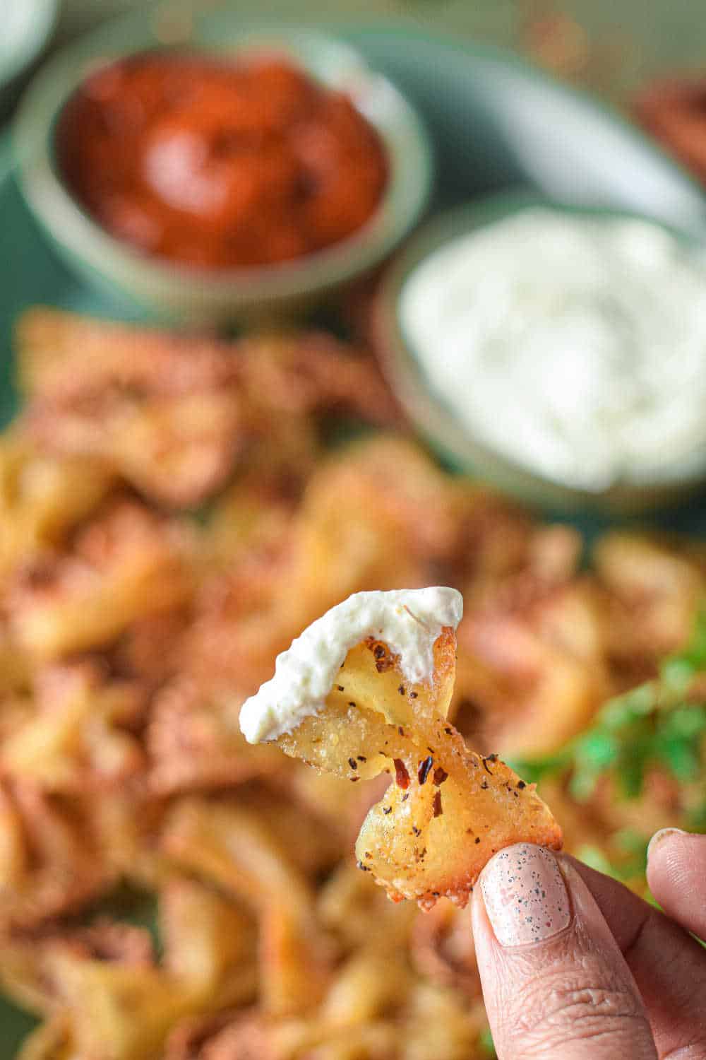 A hand holding a pasta chip with feta dip on it