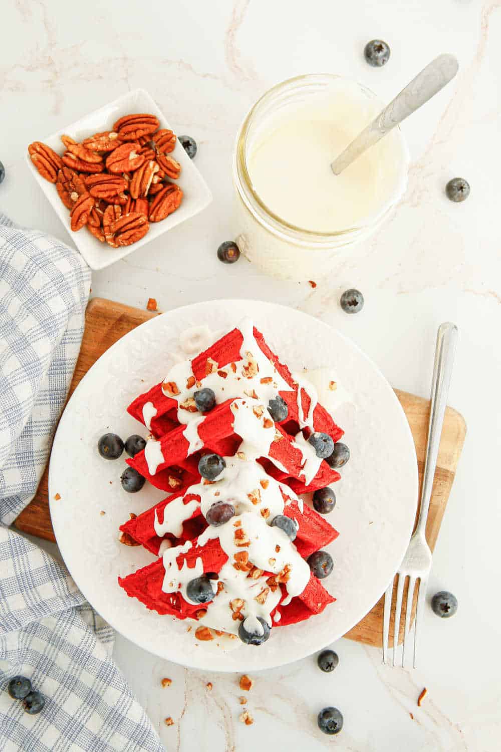 red velvet waffles with cream cheese topping on a plate with blueberries and chopped pecans.