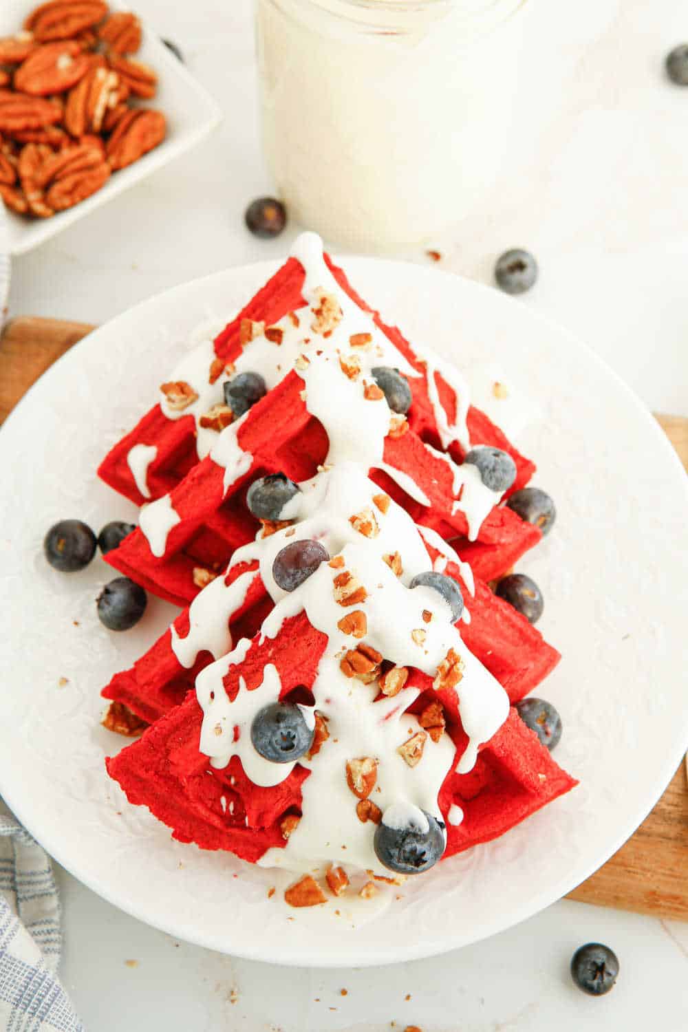 red velvet waffles on a plate covered in cream cheese topping, blueberries and pecans.