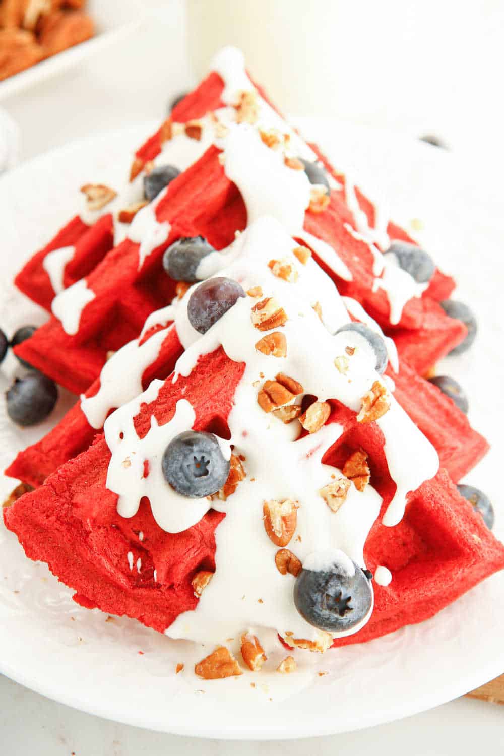red velvet waffles served on a plate with cream cheese topping, blueberries and pecans.
