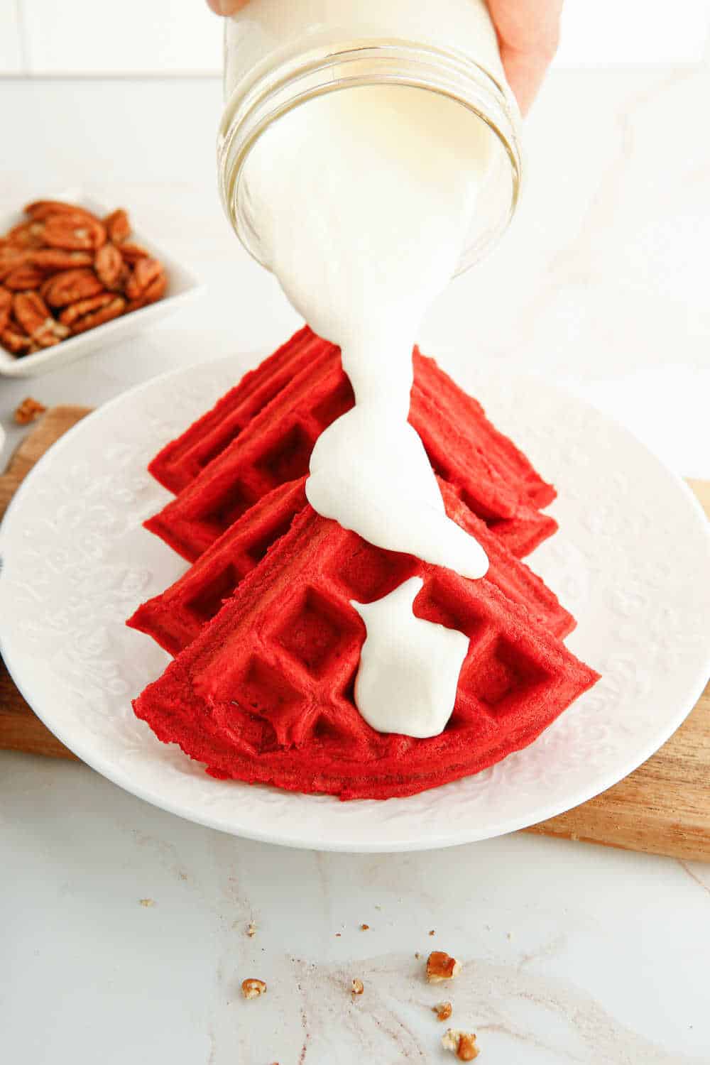 cream cheese topping being poured on red velvet waffles.