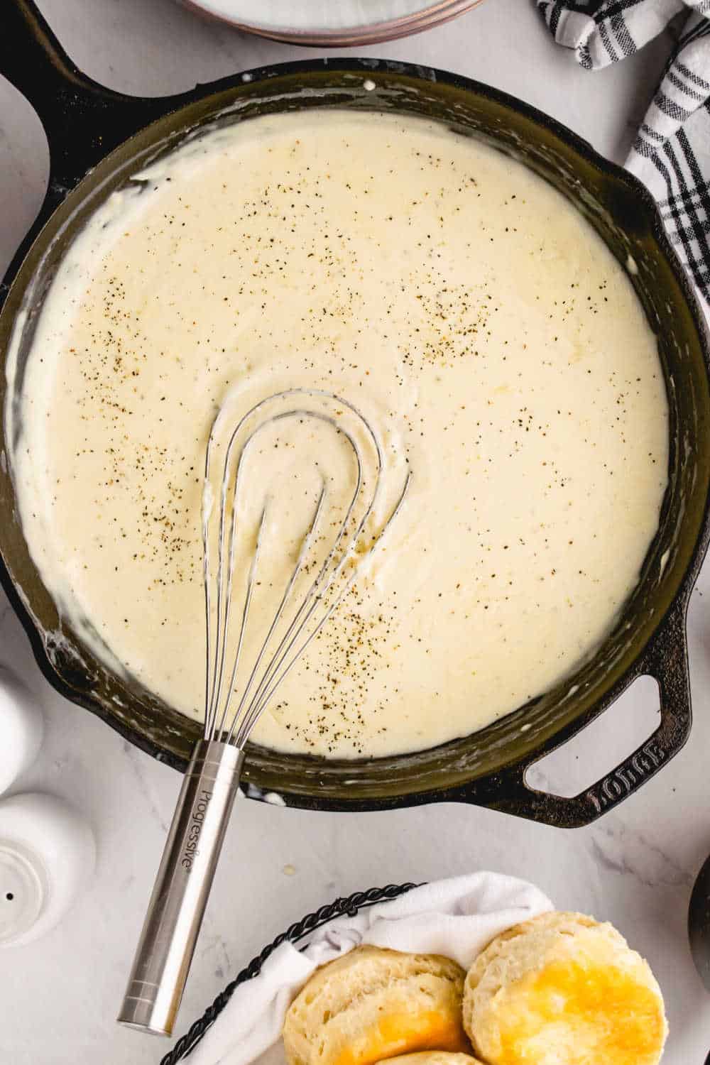 A black skillet with country gravy and a whisk.