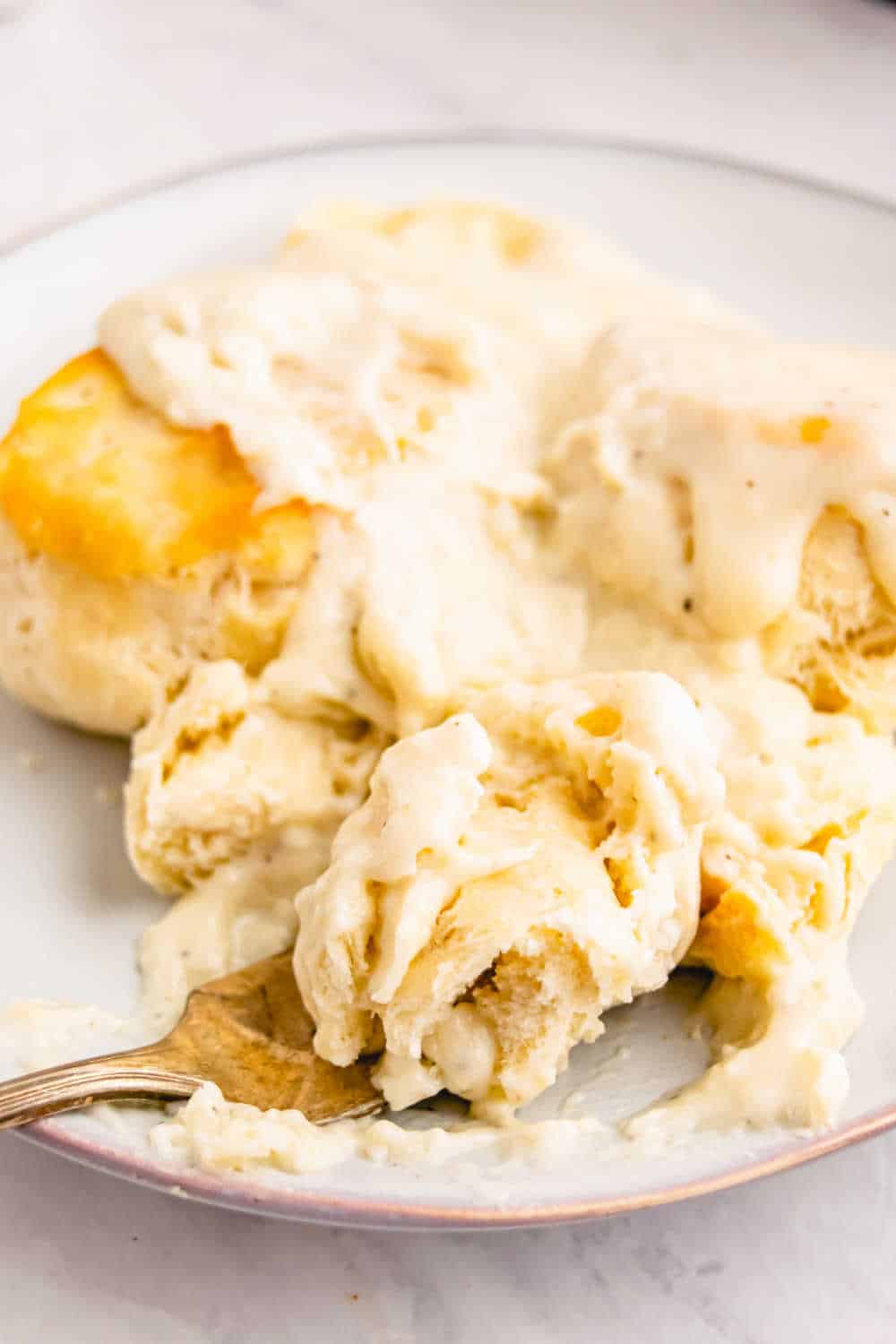 Country gravy over biscuits on a plate with a fork.