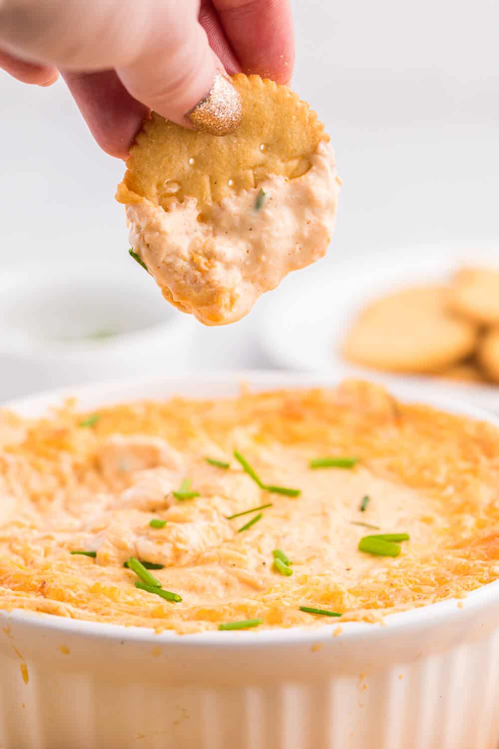 A hand holding a cracker with crab dip on it.