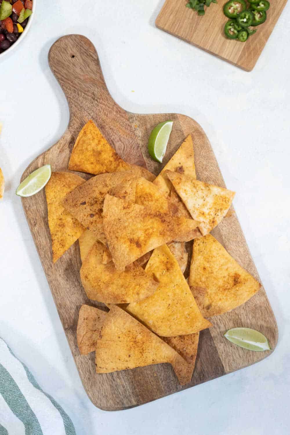 Tortilla chips on a wooden cutting board with cut limes.