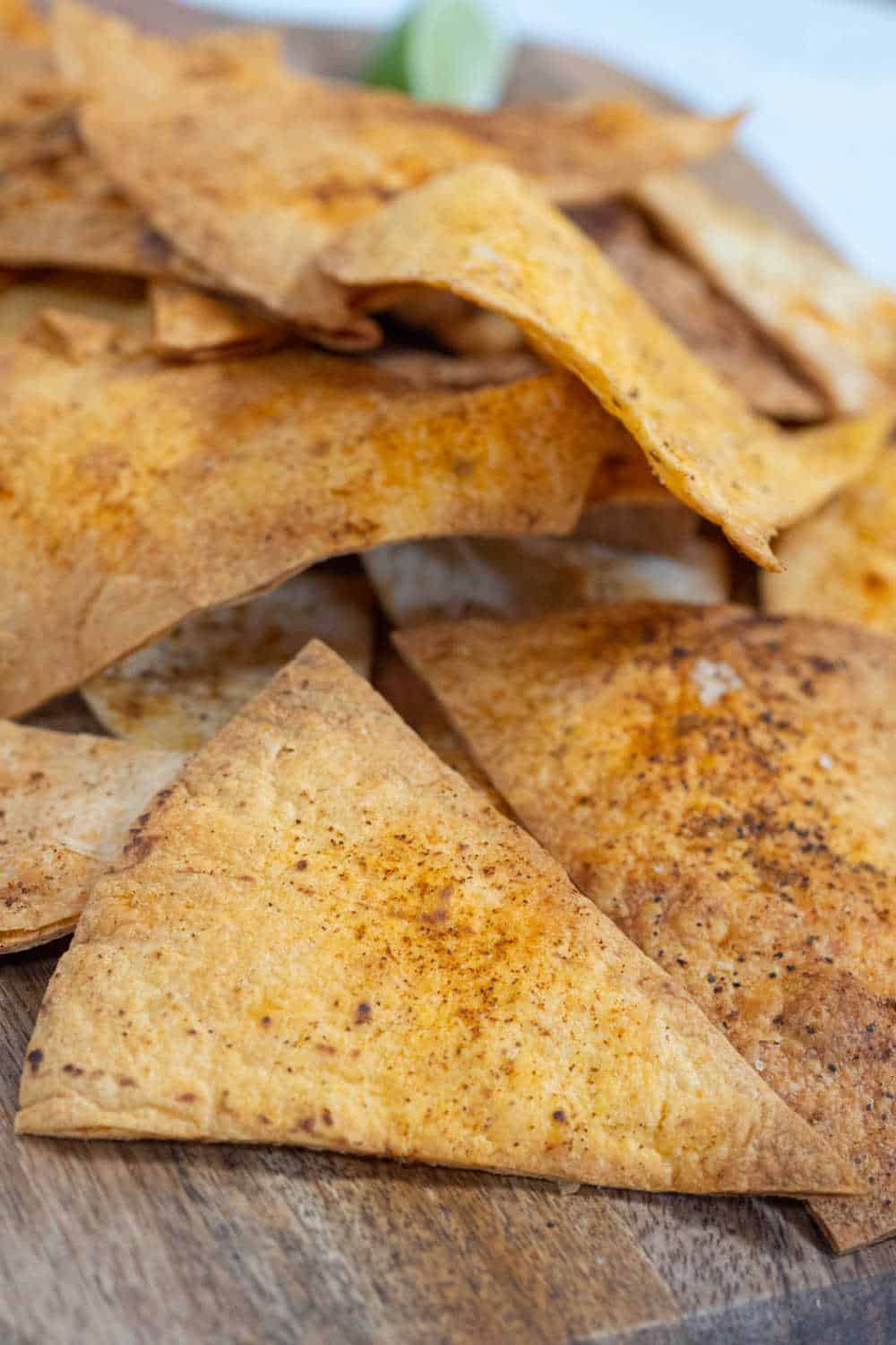 A bunch of homemade tortilla chips on a wooden board.