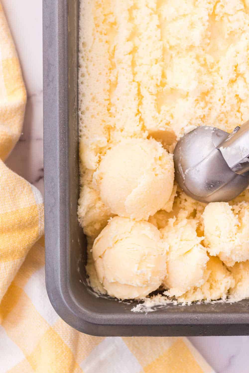 Orange sherbet in a loaf pan with an ice cream scoop.