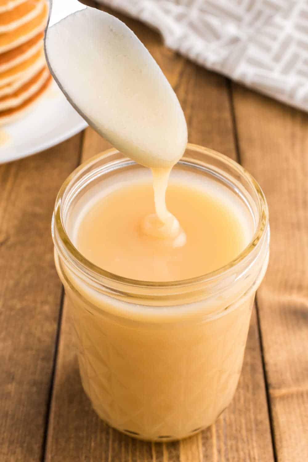 A spoon over a mason jar of pancake syrup.