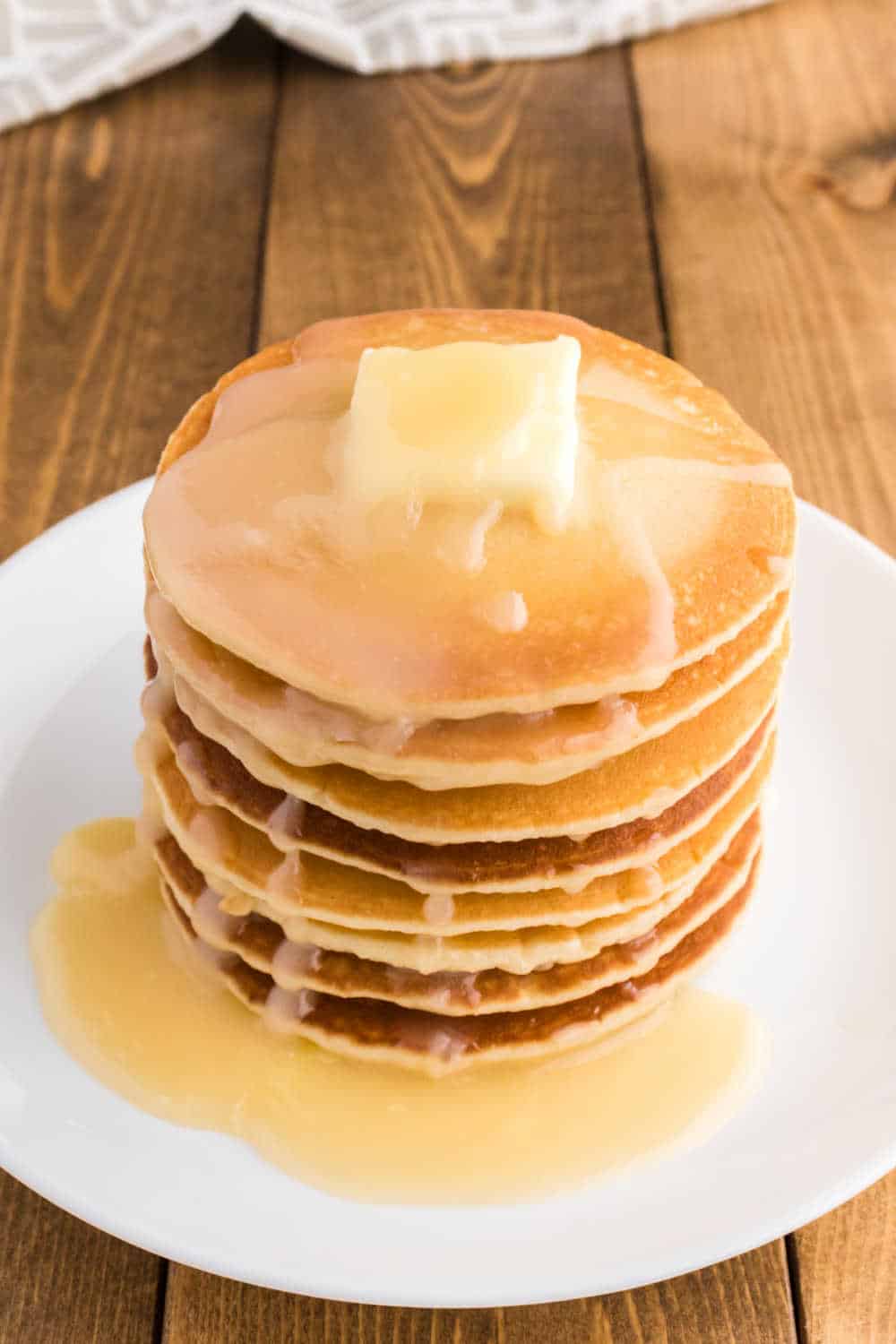 A stack of pancakes with pancake syrup on a plate.