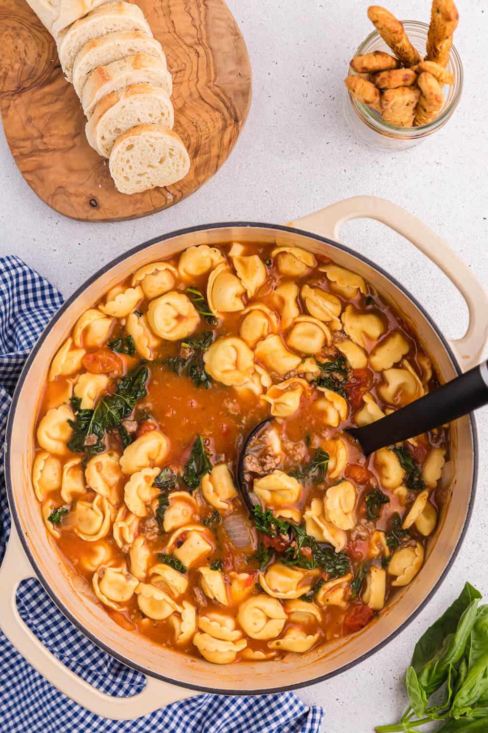 A dutch oven with tortellini soup and a black ladle.