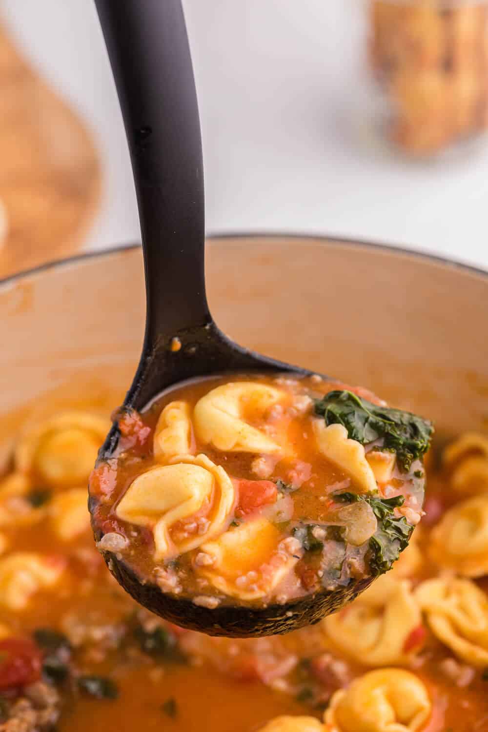 Tortellini soup in a black ladle.