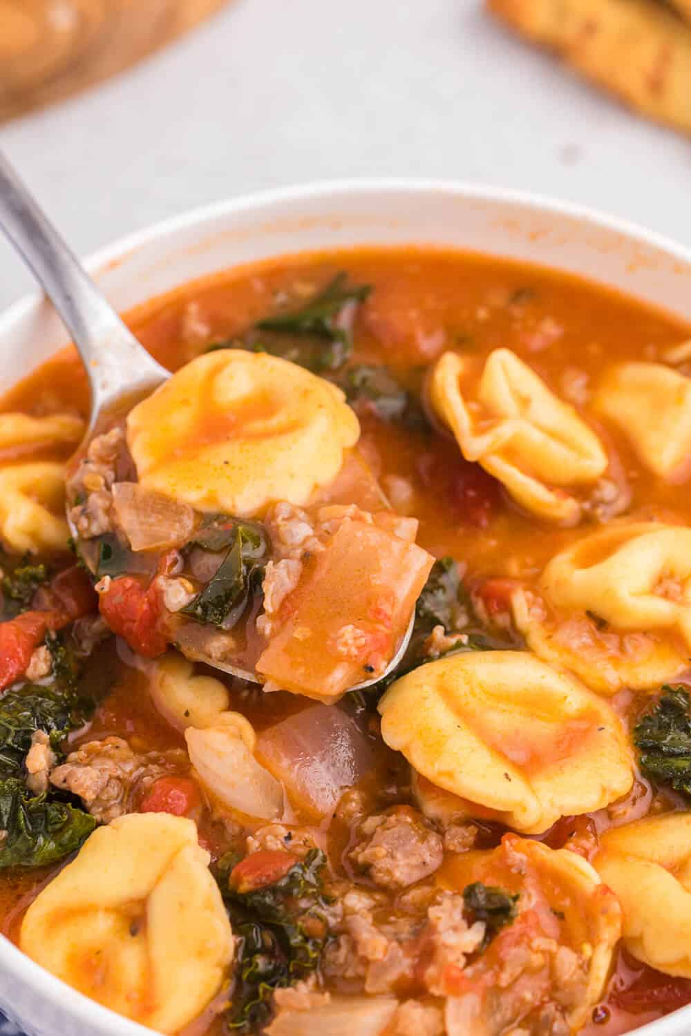 Tortellini soup on a spoon in a white bowl.