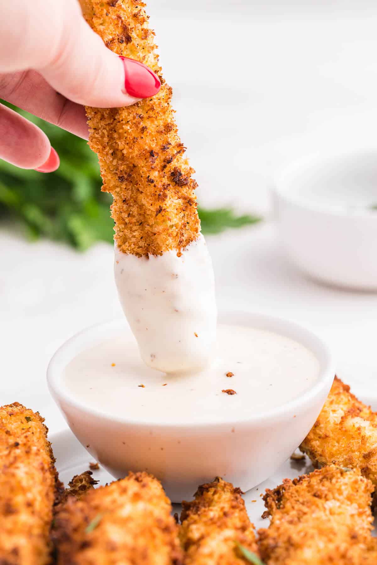 A hand dipping a fried pickle spear in ranch dressing.