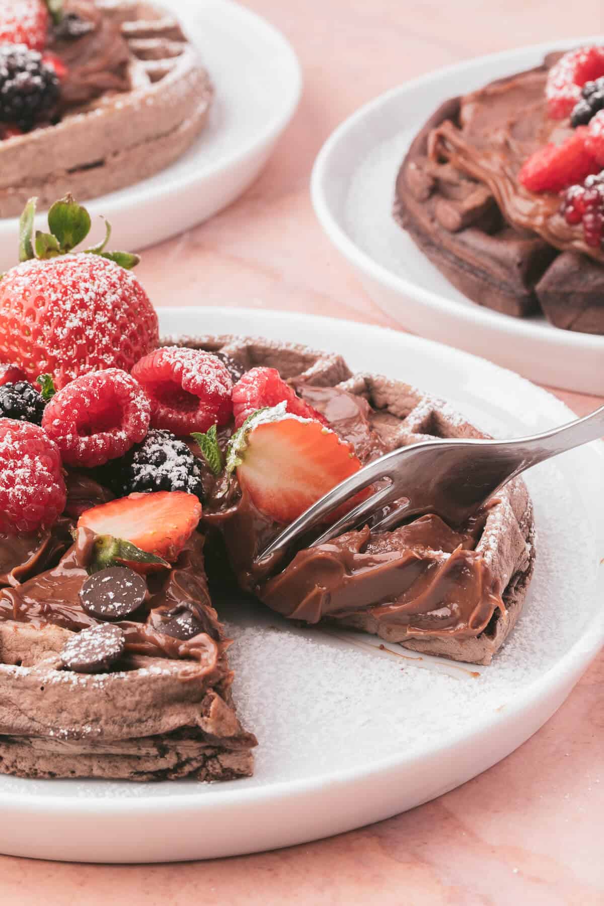 A chocolate waffle with a piece cut out and a fork in it.