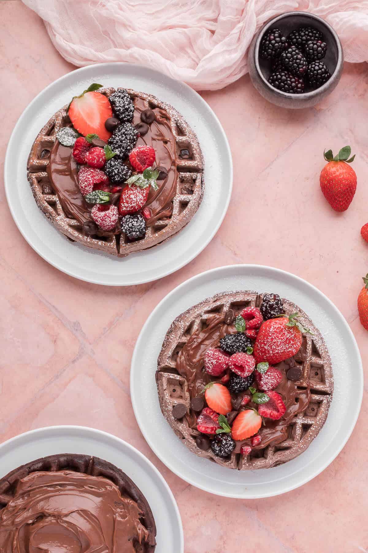 Chocolate waffles on a plate with chocolate sauce and berries.
