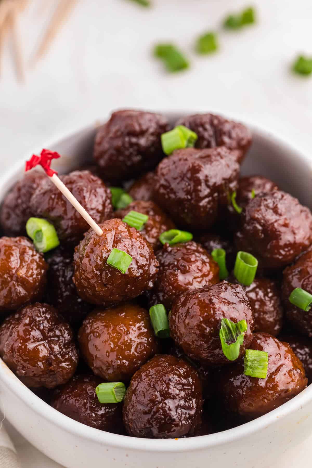 Grape jelly meatballs in a bowl with a toothpick in one meatball.