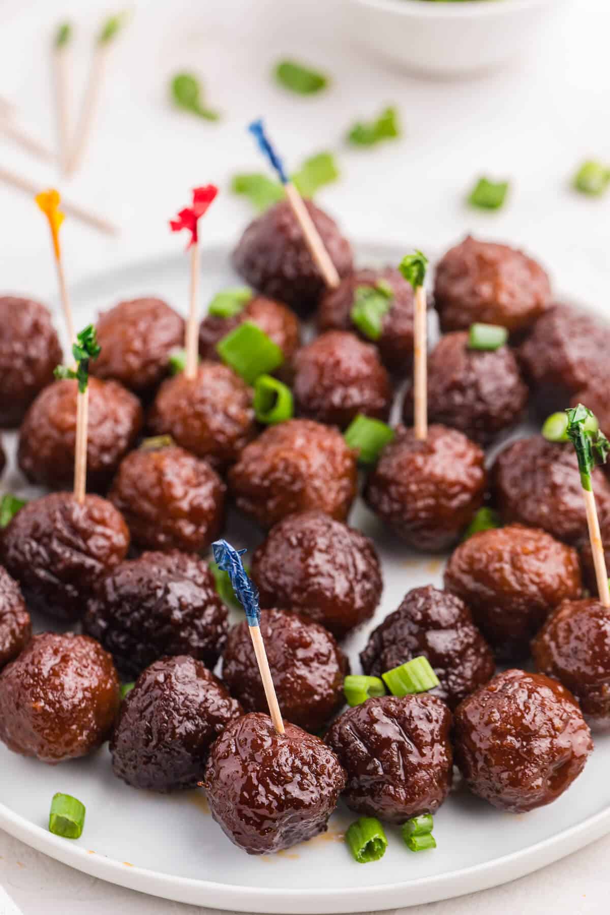 Grape jelly meatballs on a plate with toothpicks in some meatballs.