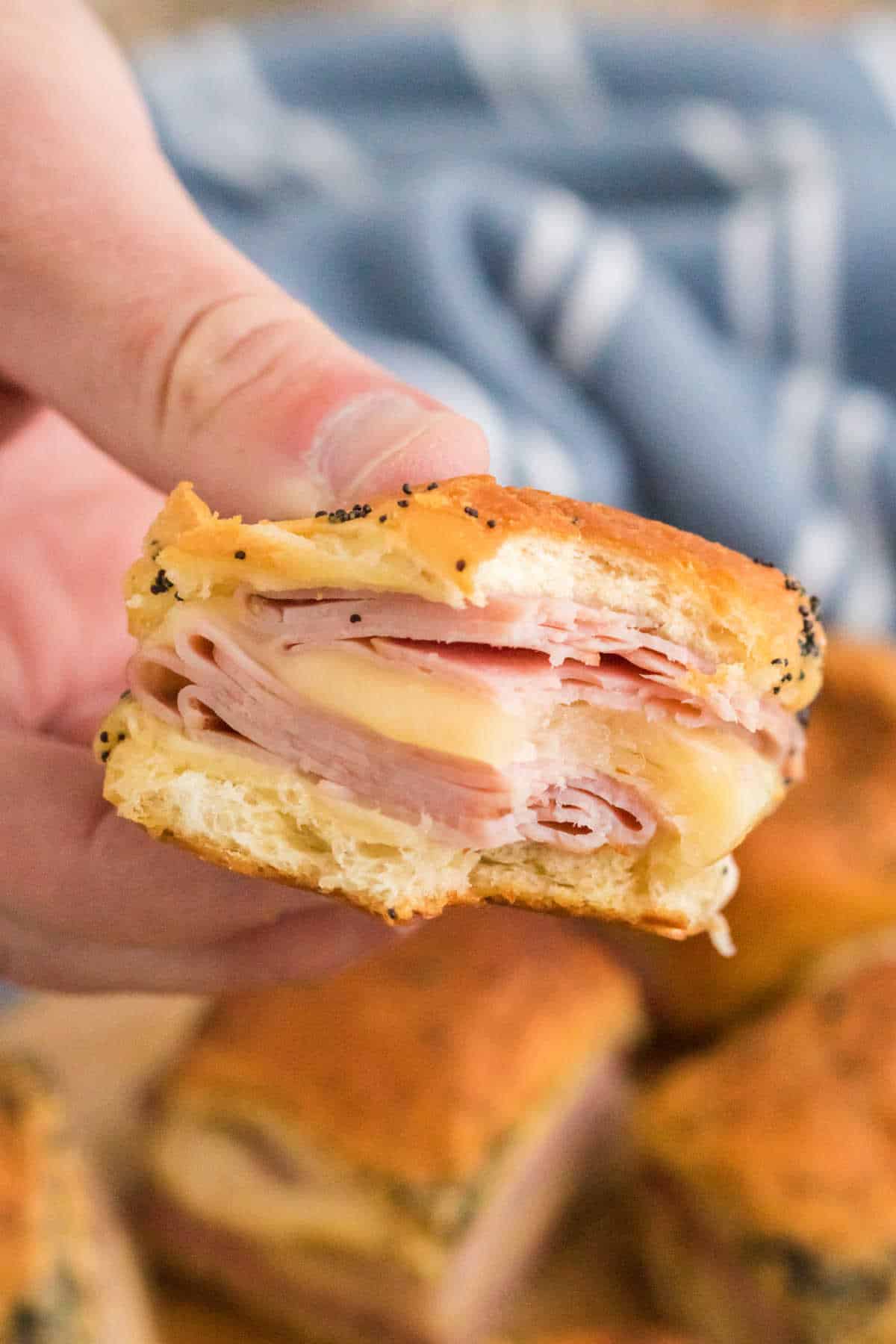 A hand holding a ham and cheese slider with a bite out of it.