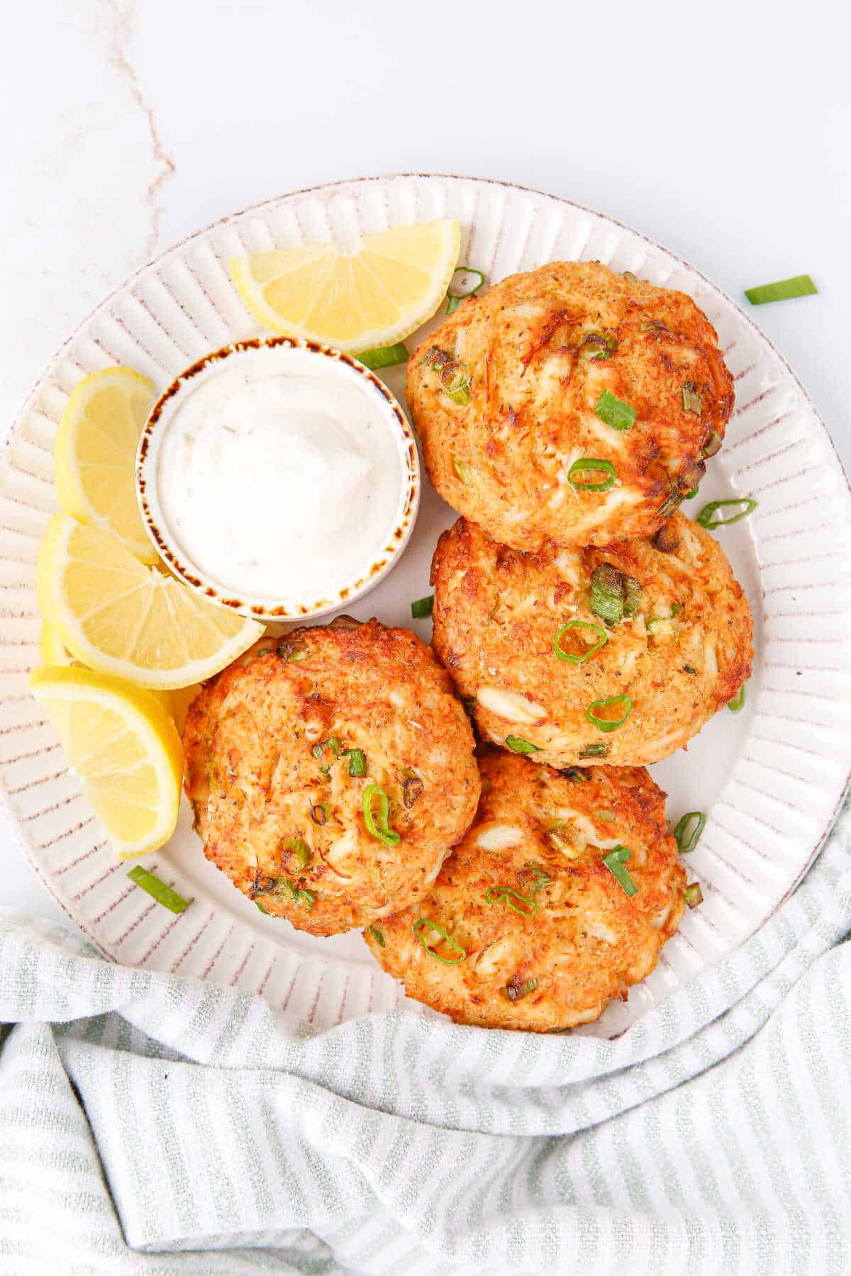 Air fryer crab cakes on a plate with tartar sauce and lemon wedges.